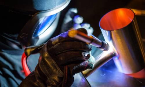 A man using a TIG (Tungsten Inert Gas) welder in a workshop.